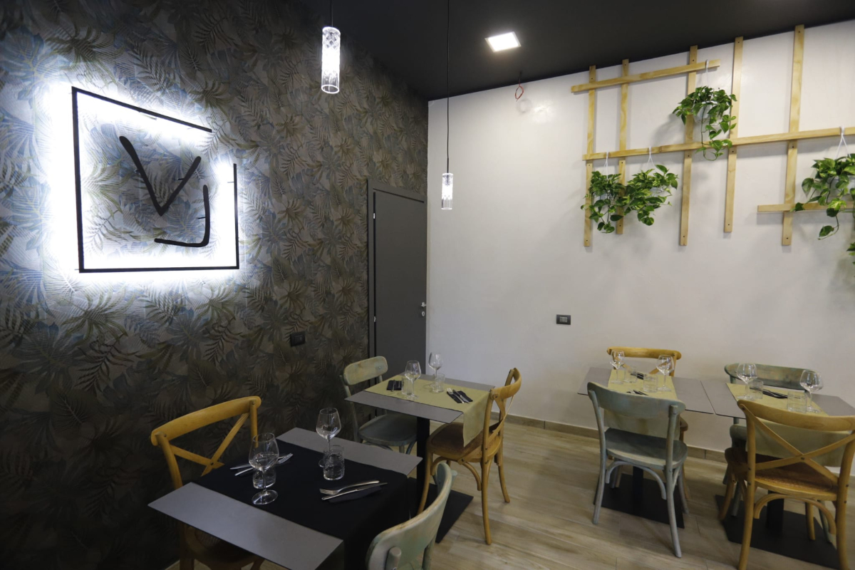 Voglia Trattoria Contemporanea, tavoli apparecchiati, sedie, insegna e decorazione floreale | LocaliArreda