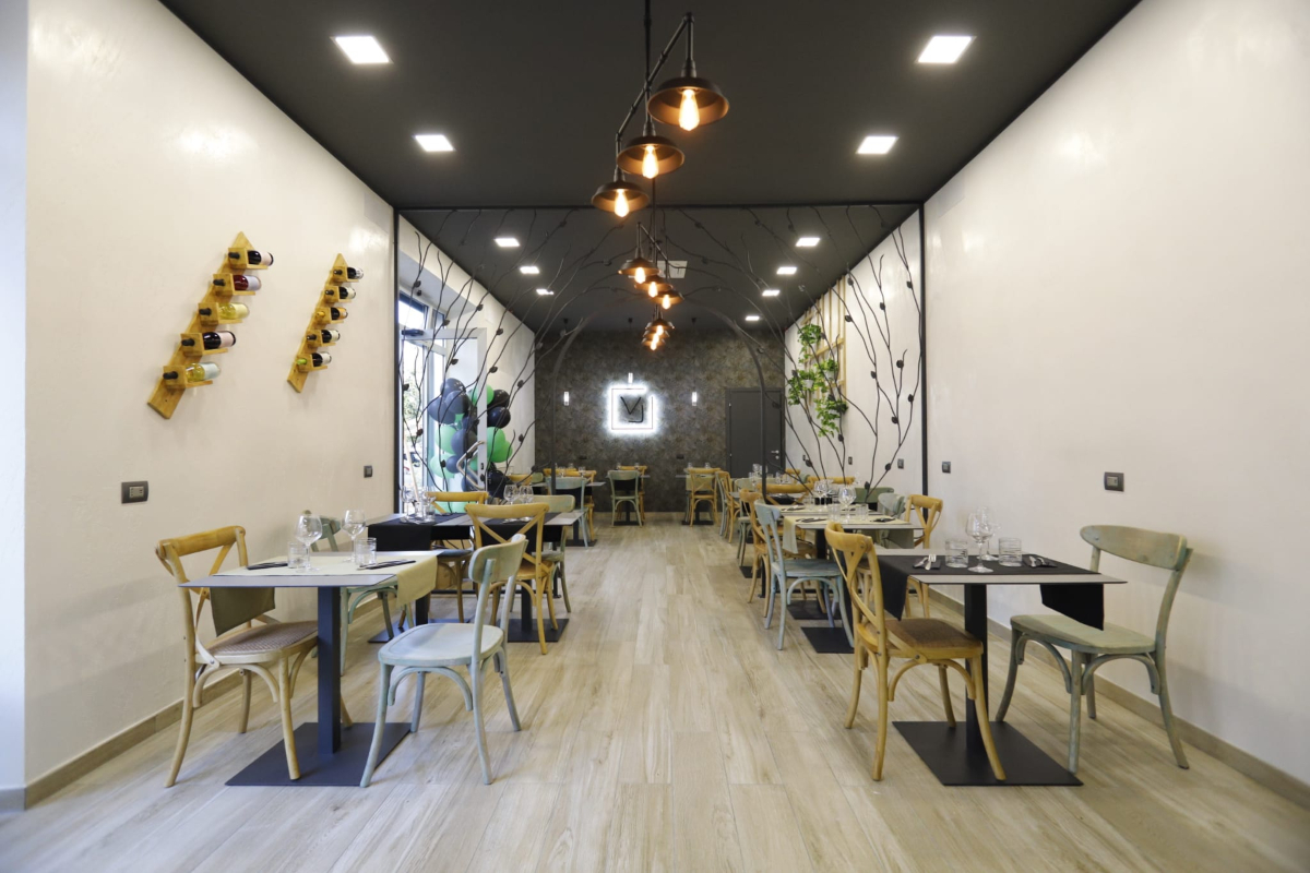 Voglia Trattoria Contemporanea, sala con tavoli apparecchiati e sedie, illuminazione a soffitto | LocaliArreda