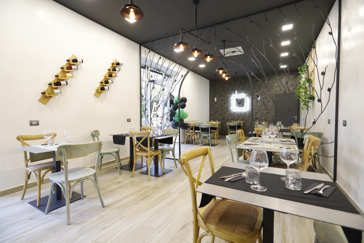 Voglia Trattoria Contemporanea, sala con tavoli apparecchiati e sedie e cancello in ferro | LocaliArreda