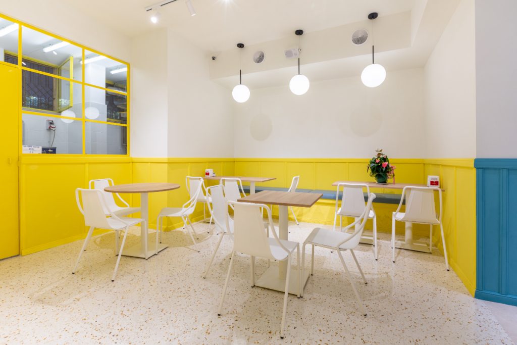 Caffetteria gelateria Gelatik, sala giallo pastello con tavolini, sedie e vista sul laboratorio