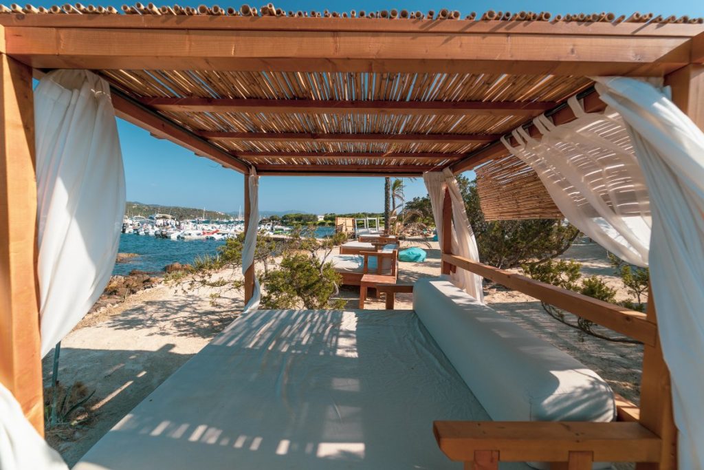 Ristorante, Lido, Stabilimento balneare The Bay (Costa Smeralda) gazebo divano in legno con copertura di canne sulla spiaggia