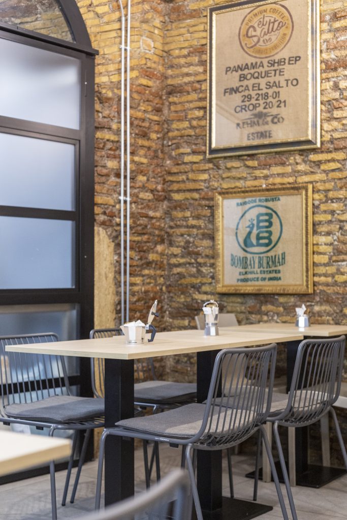 Bar bistrot Tre Caffè, tavolini e sedie con caffettiere parete con mattoni a vista